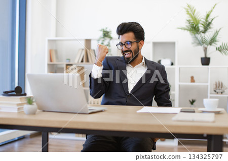 An Indian businessman is celebrating a success while working on his laptop in the office An Indian businessman is celebrating a success while working on his laptop in the office 134325797