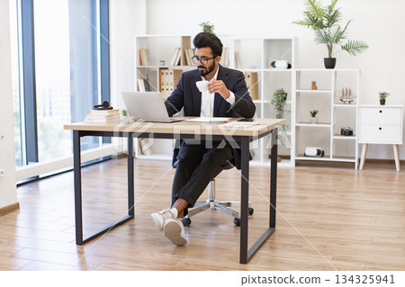 An Arab businessman is working on his laptop while drinking coffee in his modern office An Arab businessman is working on his laptop while drinking coffee in his modern office 134325941