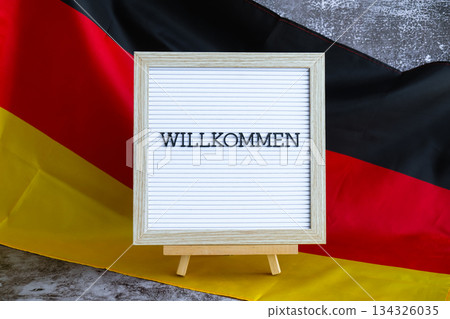 Letter board with message WILLKOMMEN Welcome National symbol of Germany. German wave silky flag background. Travel destination and tourism  134326035