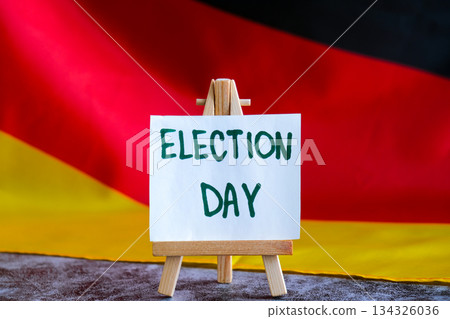 Paper note with words ELECTION DAY on National symbol of Germany. German wave silky flag background. Ellection political participation campaign and civic engagement 134326036