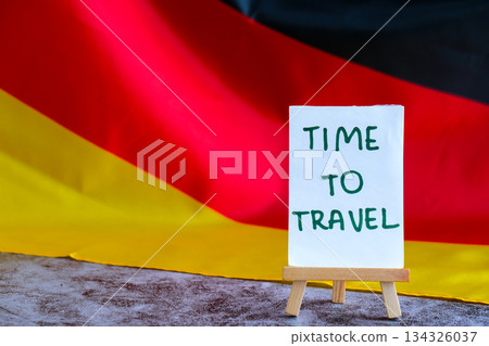 Paper note with words TIME TO TRAVEL on National symbol of Germany. German wave silky flag background. Travel destination tourism Paper note with words TIME TO TRAVEL on National symbol of Germany. German wave silky flag background. Travel destination tourism 134326037