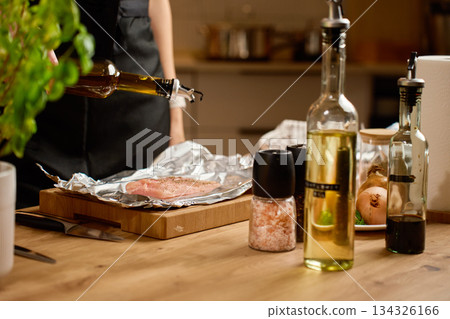 Woman pouring olive oil on raw chicken breast on kitchen table 134326166