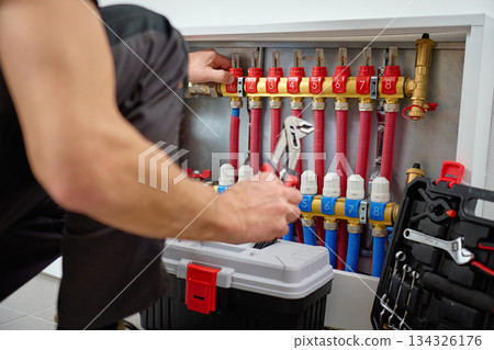 Technician adjusting underfloor heating manifold with valves and pipes 134326176