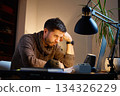 Fatigued man sitting at home desk looking at laptop 134326229
