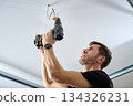 Man drilling ceiling with cordless power drill indoors 134326231
