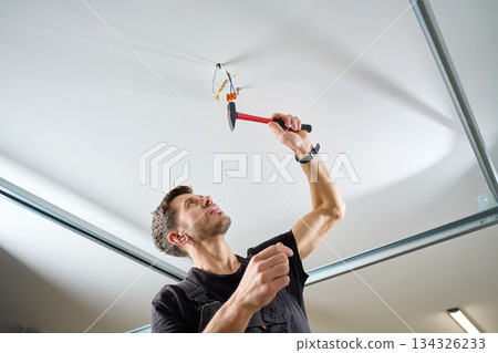 Man hammering nail-in anchor into ceiling Man hammering nail-in anchor into ceiling 134326233