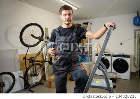 Handyman holding drill standing on ladder in utility room Handyman holding drill standing on ladder in utility room 134326235