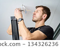 Man connecting electrical wires while installing ceiling light indoors 134326236