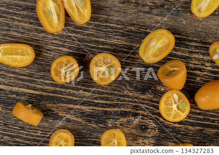 lots of ripe orange kumquat in half on a wooden table, a group of scattered and sliced kumquat fruits on a wooden table and board lots of ripe orange kumquat in half on a wooden table, a group of scattered and sliced kumquat fruits on a wooden table and board 134327283