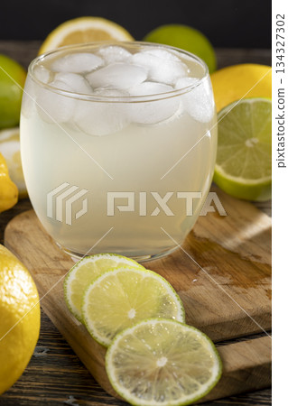 cold lemon drink with the addition of pieces of pure ice in a glass, sweet drink with lemon flavor and whole juicy lemons and limes 134327302