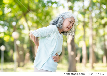 Old asian woman grandmother patient hands holding stomach in pain while walking outdoors in the park Old asian woman grandmother patient hands holding stomach in pain while walking outdoors in the park 134327437
