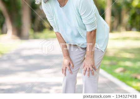 Old woman grandmother patient hands holding knee in pain or tired while walking outdoors in the park 134327438