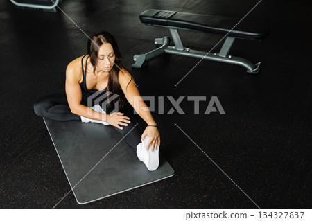 Woman is stretching body in gym. portrait and sport preparation. Young woman is stretching her leg in gym 134327837