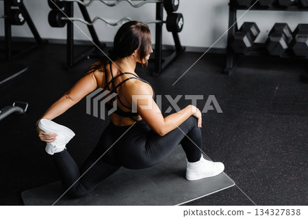 Woman is stretching body in gym. portrait and sport preparation. Young woman is stretching her leg in gym Woman is stretching body in gym. portrait and sport preparation. Young woman is stretching her leg in gym 134327838