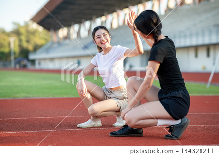 Asian woman clapping hands high five friend as sitting crouching on running track in sports stadium. Asian woman clapping hands high five friend as sitting crouching on running track in sports stadium. 134328211