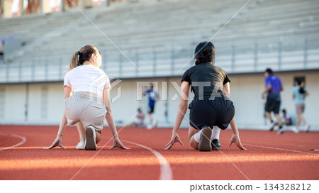 Back view shot of asian woman and friend sitting crouching before running on track in sports stadium 134328212