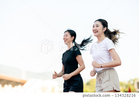Happy asian woman and a friend running jogging together on racetrack in sports stadium on sunny day. Happy asian woman and a friend running jogging together on racetrack in sports stadium on sunny day. 134328216