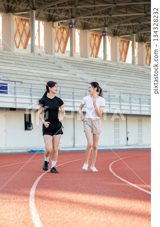 Asian woman friends running or jogging together on racetrack exercising outdoors in sports stadium 134328232
