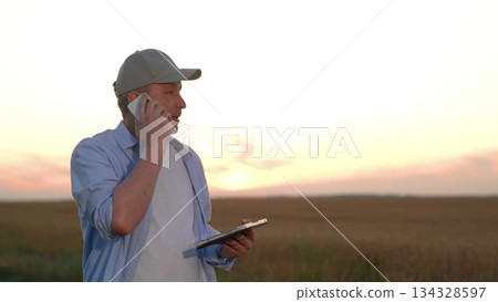 Farmer talking smartphone wheat field, male farmer worker phone sunset, hand holding digital tablet, business success industry, farm owner reviewing app in sunset glow, smart farming technology in 134328597