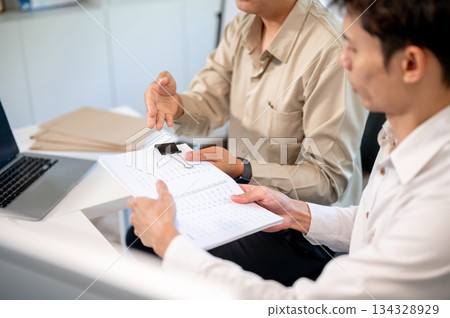 Close up of asian businessman looking and handing document to coworker at table in company's office. 134328929