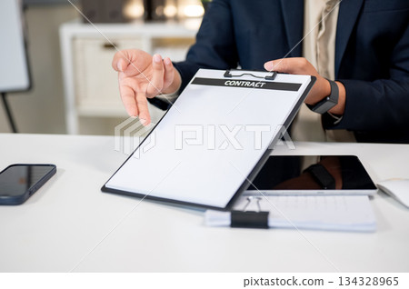 Close up of businessman's hand pointing at contract document on clipboard at table in company office 134328965
