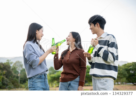 Asian friends woman and man standing and enjoy drinking alcohol in field with mountain view and sky. 134329377
