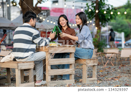 Asian women and man friend clinking drink bottles while sitting on crate in a campground restaurant. Asian women and man friend clinking drink bottles while sitting on crate in a campground restaurant. 134329397