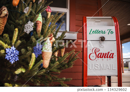 Santa mailbox beside a decorated Christmas tree with colorful ornaments in an outdoor holiday setting. 134329602