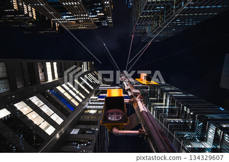 A glowing traffic light rises through the center of towering glass buildings, with cables stretching like spider silk into the night sky 134329607