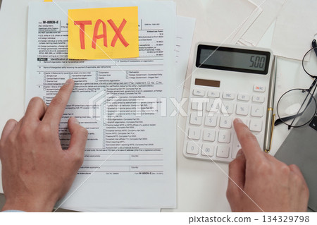 Tax Filing Process. Individual preparing tax forms with calculator and notes. Tax Filing Process. Individual preparing tax forms with calculator and notes. 134329798
