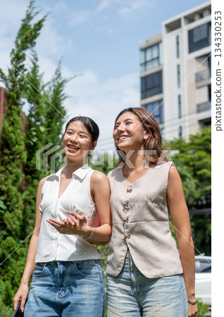 Pretty asian woman couple friends holding hands standing or walking together in hot summer sunlight. Pretty asian woman couple friends holding hands standing or walking together in hot summer sunlight. 134330253