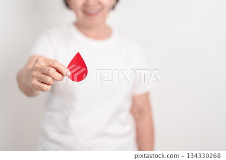 Elderly woman with red Blood drop paper for concept of June World Blood Donor day, Donation, January Blood donor awareness month, April Hemophilia awareness day, May Thalassemia Day, Anemia awareness Elderly woman with red Blood drop paper for concept of June World Blood Donor day, Donation, January Blood donor awareness month, April Hemophilia awareness day, May Thalassemia Day, Anemia awareness 134330268