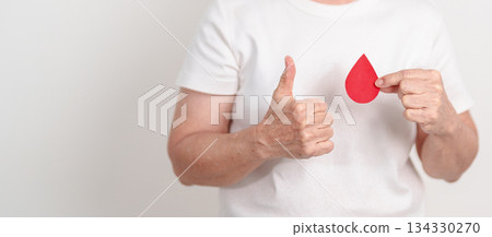 Elderly woman with red Blood drop paper for concept of June World Blood Donor day, Donation, January Blood donor awareness month, April Hemophilia awareness day, May Thalassemia Day, Anemia awareness 134330270