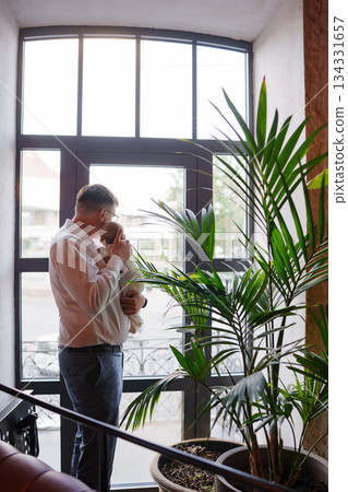 Father lovingly holds baby by the window in a cozy setting 134331657