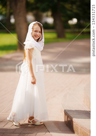 Girl in white dress smiles in a sunny park setting 134331715