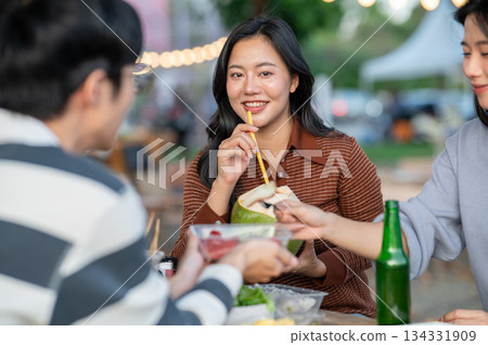 Asian woman drinking coconut water and friend eating fruit sitting at table in campground restaurant 134331909