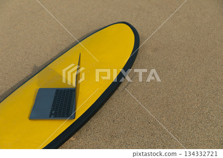 Laptop placed on surfboard on sandy beach under clear sky 134332721