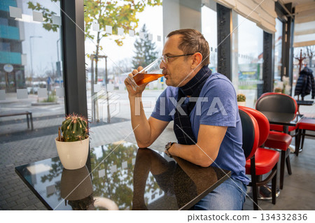 Portrait of a man drinking tea while sitting at a table in a cafe. Captures a moment of calm, reflection and everyday urban lifestyle in a public space. Portrait of a man drinking tea while sitting at a table in a cafe. Captures a moment of calm, reflection and everyday urban lifestyle in a public space. 134332836