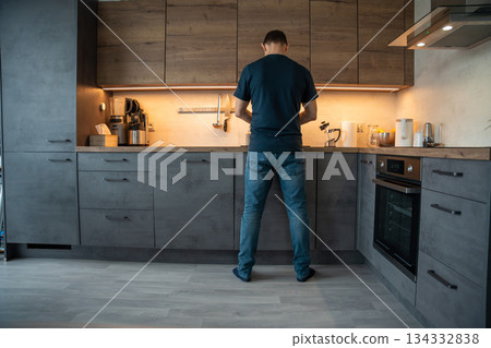 Man cooking in the kitchen while facing the stove. Home meal preparation. Man cooking in the kitchen while facing the stove. Home meal preparation. 134332838