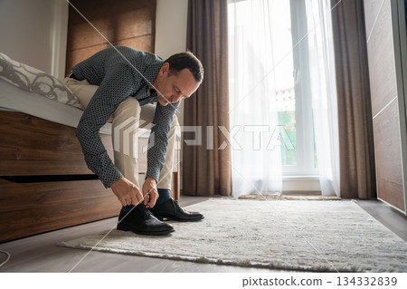 Man tying shoelaces while getting ready in the bedroom. Daily preparation before going out. 134332839