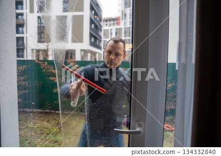 Man cleans exterior window with squeegee. Concept of seasonal cleaning and household chores. 134332840