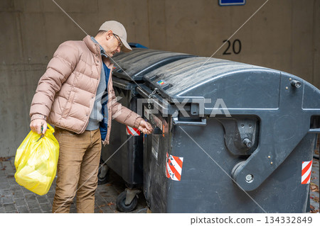 Man throwing garbage into a black dumpster outside. Waste management and everyday responsibilities. Man throwing garbage into a black dumpster outside. Waste management and everyday responsibilities. 134332849