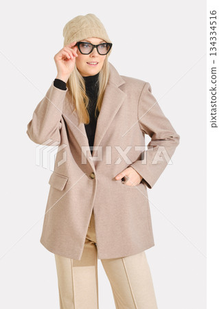 Fashionable woman wearing a stylish coat and winter hat while posing confidently indoors Fashionable woman wearing a stylish coat and winter hat while posing confidently indoors 134334516