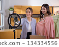 Two young asian woman live streaming online clothing store while showing clothing with smartphone. 134334556