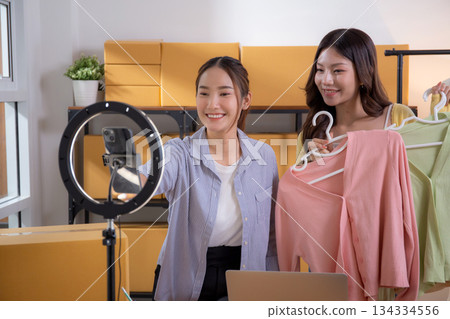 Two young asian woman live streaming online clothing store while showing clothing with smartphone. Two young asian woman live streaming online clothing store while showing clothing with smartphone. 134334556