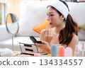 Beauty happy young asian woman applying makeup with brush looking mirror in living room. 134334557