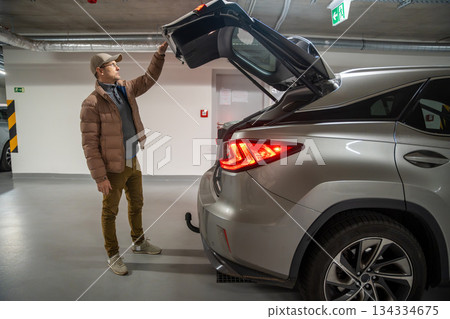 Man opening the trunk of an SUV in underground parking. Routine task before a trip or errand. 134334675