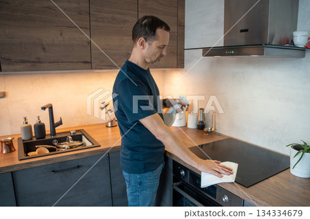 Man wiping stove surface in a kitchen. Daily cleaning routine. Man wiping stove surface in a kitchen. Daily cleaning routine. 134334679