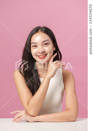 Skincare Routine. Young woman applying moisturizer with a radiant smile against a pink background. Skincare Routine. Young woman applying moisturizer with a radiant smile against a pink background. 134334870