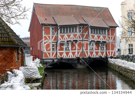 Sandbags line canal flood protection barrier historic Wismar town architecture timber facade building. Emergency safety infrastructure reinforces embankment stability high water risk overcast weather Sandbags line canal flood protection barrier historic Wismar town architecture timber facade building. Emergency safety infrastructure reinforces embankment stability high water risk overcast weather 134334944